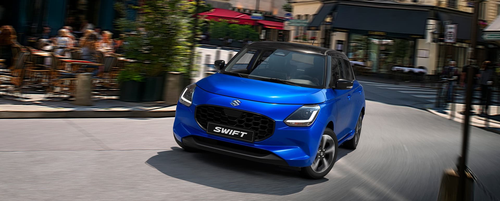 Zafírkék Suzuki Swift parkol egy forgalmas városi utcában